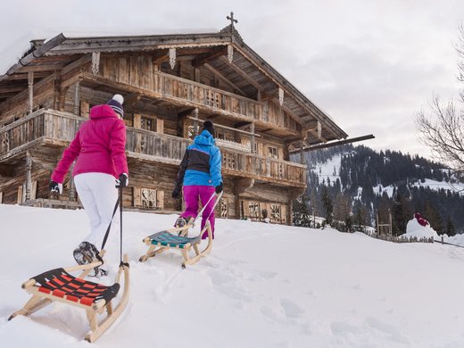 Winter in Söll: das Skigebiet SkiWelt Wilder Kaiser Zwei Personen ziehen Schlitten vor einer verschneiten Holzhütte in den Bergen