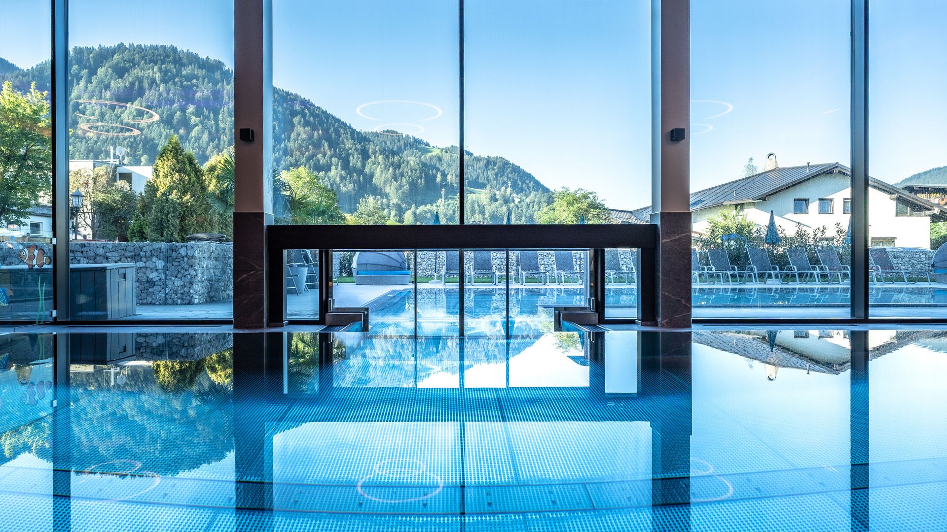 Hotel in Söll am Wilden Kaiser: der Postwirt Innen- und Außenpool mit Bergblick durch große Fenster