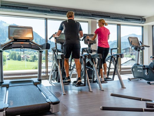 Sie suchen ein Hotel mit Fitnessstudio in Österreich? Mann und Frau trainieren auf Crosstrainern in einem Fitnessstudio mit Panoramablick