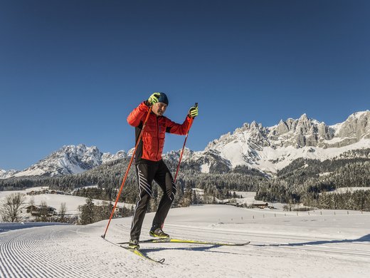 Postwirt Söll: Ihr Langlaufhotel in Tirol Mann beim Langlaufen auf präparierter Strecke vor verschneiten Bergen und blauem Himmel