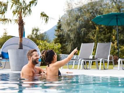 Ihre Traumtage im Postwirt Söll Paar entspannt im Pool, Frau zeigt lachend in die Ferne