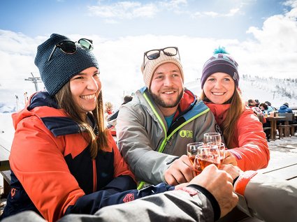 Winter in Söll: das Skigebiet SkiWelt Wilder Kaiser Freunde stoßen mit Getränken im Schnee bei sonnigem Winterwetter an