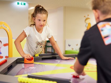 Spaß und Action im Kinderhotel in Söll Mädchen und Junge spielen lustiges Tischspiel in bunter Kinderspielhalle