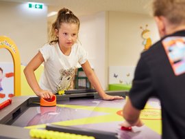 Kinder spielen Airhockey im Hotel Ein Kind spielt konzentriert Airhockey im Freizeitbereich eines Hotels, während ein Erwachsener im Hintergrund steht.
