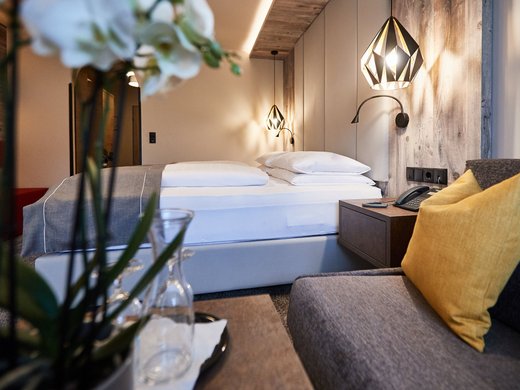Unser Hotel in Söll/Österreich: eine spannende Geschichte Modernes Hotelzimmer mit Bett, Sitzbereich und stilvoller Beleuchtung
