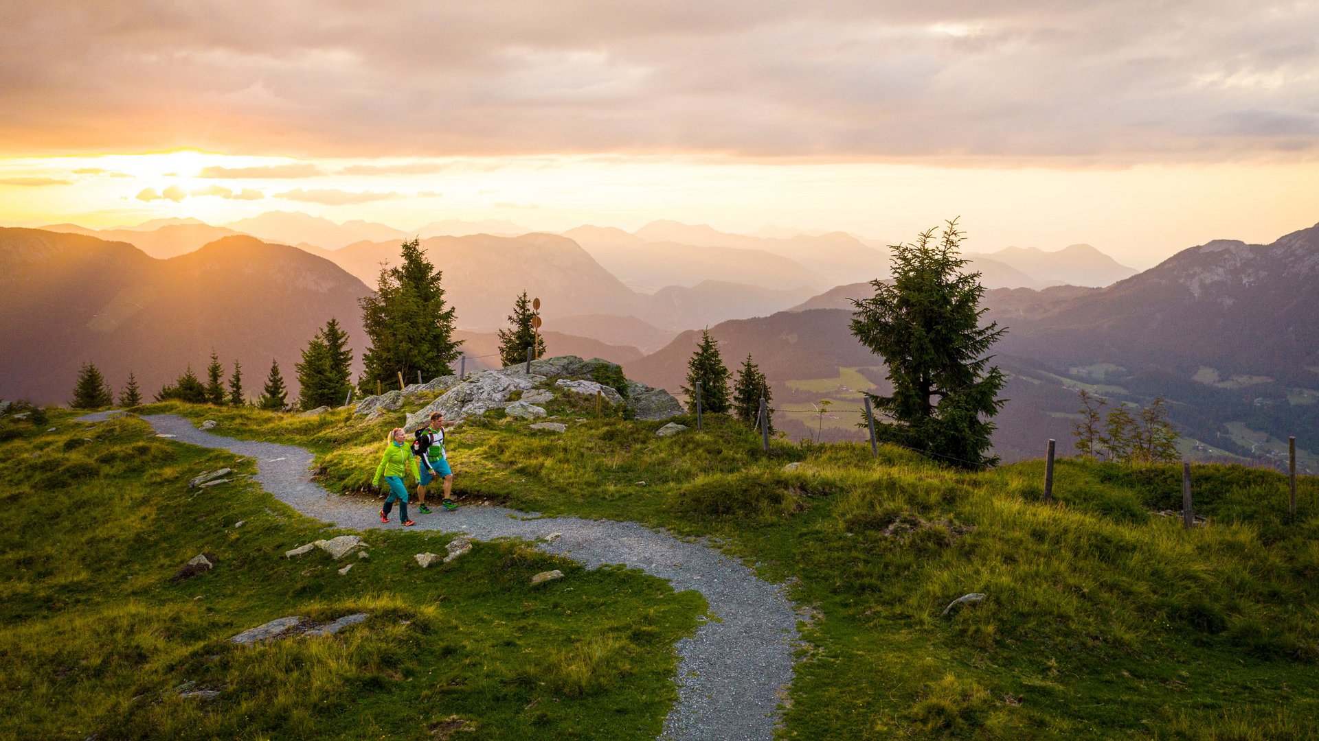 Entdecken Sie die Region mit der Wilder Kaiser GästeCard! Zwei Wanderer auf einem Pfad bei Sonnenuntergang in den Bergen