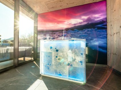 Eisbrunnen im Spa mit Bergpanorama Moderner Eisbrunnen im Spa-Bereich, beleuchtet mit bunten Lichtern, mit Panoramablick auf die Berge und Sonnenlicht, das durch die Fenster scheint.