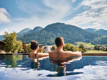 Der Postwirt: Hotel mit Infinitypool in Tirol Paar entspannt im Pool mit Bergblick unter blauem Himmel