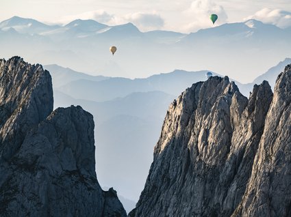 Entdecken Sie die Region mit der Wilder Kaiser GästeCard! Heiße Luftballons über felsigen Bergen mit einem nebeligen Bergpanorama im Hintergrund
