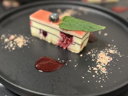 Kulinarische Verführungen in unserem Hotel in Söll/Tirol Schichtdessert mit Beerensauce, Blaubeere und Minzblatt auf schwarzem Teller