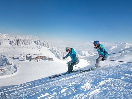 Winter in Söll: das Skigebiet SkiWelt Wilder Kaiser Zwei Skifahrer fahren auf verschneiter Skipiste bei klarem Himmel