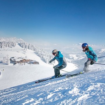 Urlaub in Söll mit Kindern oder als Pärchen Zwei Skifahrer fahren auf verschneiter Skipiste bei klarem Himmel