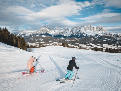 Winter in Söll: das Skigebiet SkiWelt Wilder Kaiser Zwei Skifahrer auf einer präparierten Piste mit verschneiten Bergen im Hintergrund