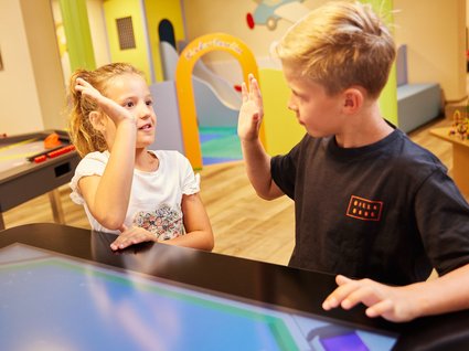 Spaß und Action im Kinderhotel in Söll Zwei Kinder geben sich in einem Spielzimmer einen High-Five