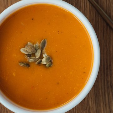 Urlaub in Söll mit Kindern oder als Pärchen Kürbissuppe mit Kürbiskernen in einer weißen Schüssel auf Holztisch