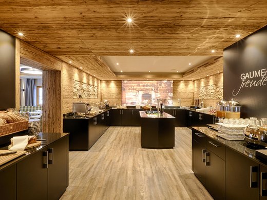 Unser Hotel in Söll/Österreich: eine spannende Geschichte Moderne Frühstückstheke mit Brot und Getränken in warm beleuchtetem Raum