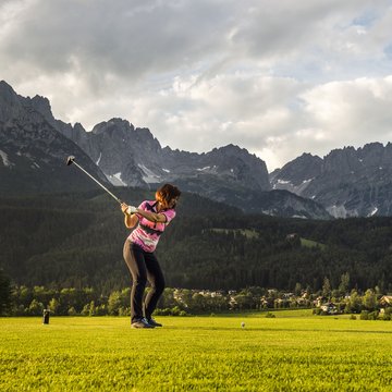 Urlaub in Söll mit Kindern oder als Pärchen Frau spielt Golf vor einer Berglandschaft mit bewölktem Himmel