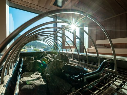 Sie suchen ein Wellnesshotel in Tirol für adults only? Saunaofen mit Steinen und Sonnenlicht durch das Fenster im Holzsaunaraum