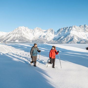 Urlaub in Söll mit Kindern oder als Pärchen Zwei Personen bei Winterwanderung im Schnee vor verschneiten Bergen und blauem Himmel