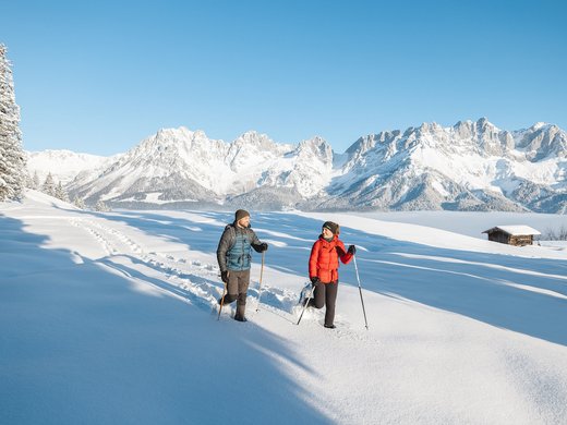 Winter in Söll: das Skigebiet SkiWelt Wilder Kaiser Zwei Personen bei Winterwanderung im Schnee vor verschneiten Bergen und blauem Himmel