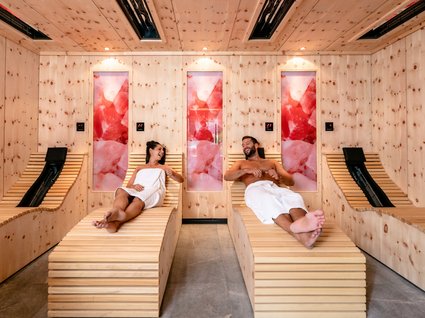 Day Spa in Söll: Kurzurlaub in Tirol Zwei Personen entspannen in einem modernen Holzsauna-Ruheraum mit rosa Wanddekorationen.