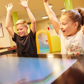 Urlaub in Söll mit Kindern oder als Pärchen Zwei Kinder spielen an einem interaktiven Touchscreen mit erhobenen Armen
