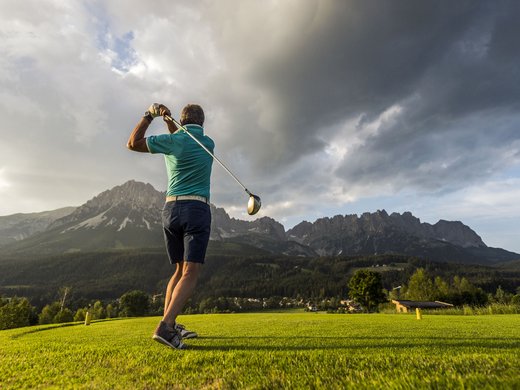 Sommer am Wilden Kaiser: Wandern und mehr Mann spielt Golf vor einer Berglandschaft mit dramatischem Himmel