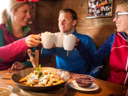 Winter in Söll: das Skigebiet SkiWelt Wilder Kaiser Drei Freunde stoßen mit heißen Getränken an, Person vor Pfannengericht mit Soße