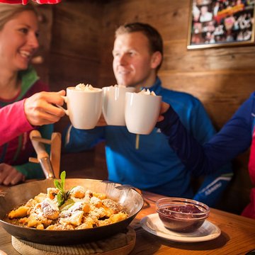 Urlaub in Söll mit Kindern oder als Pärchen Drei Freunde stoßen mit heißen Getränken an, Person vor Pfannengericht mit Soße