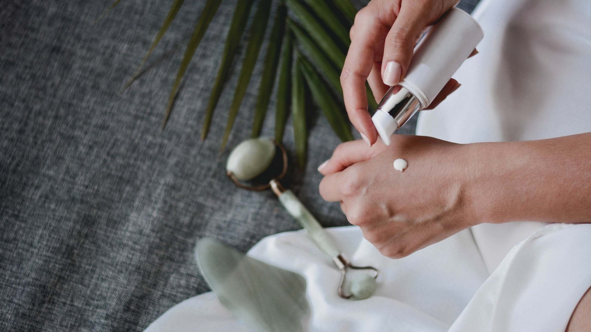 Wunderbare Wellness in Söll am Wilden Kaiser Hände tragen Creme auf, mit Jade-Gesichtsroller und Pflanzenblatt im Hintergrund