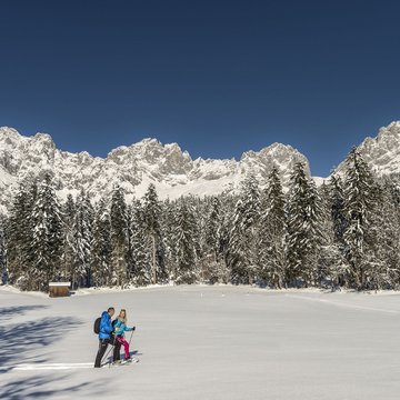 Urlaub in Söll mit Kindern oder als Pärchen Zwei Skifahrer in blauer Winterkleidung im verschneiten Gebirge vor Tannenwald