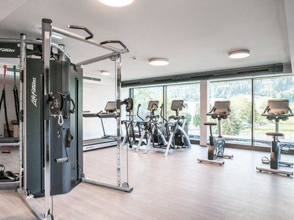 Sie suchen ein Hotel mit Fitnessstudio in Österreich? Moderner Fitnessraum mit Geräten und großem Fenster mit Bergblick