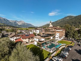 Hotelanlage mit Pool und Alpenblick Luftaufnahme eines Hotels mit Außenpool, umgeben von Bergen und malerischer Landschaft, in einer ruhigen alpinen Umgebung.