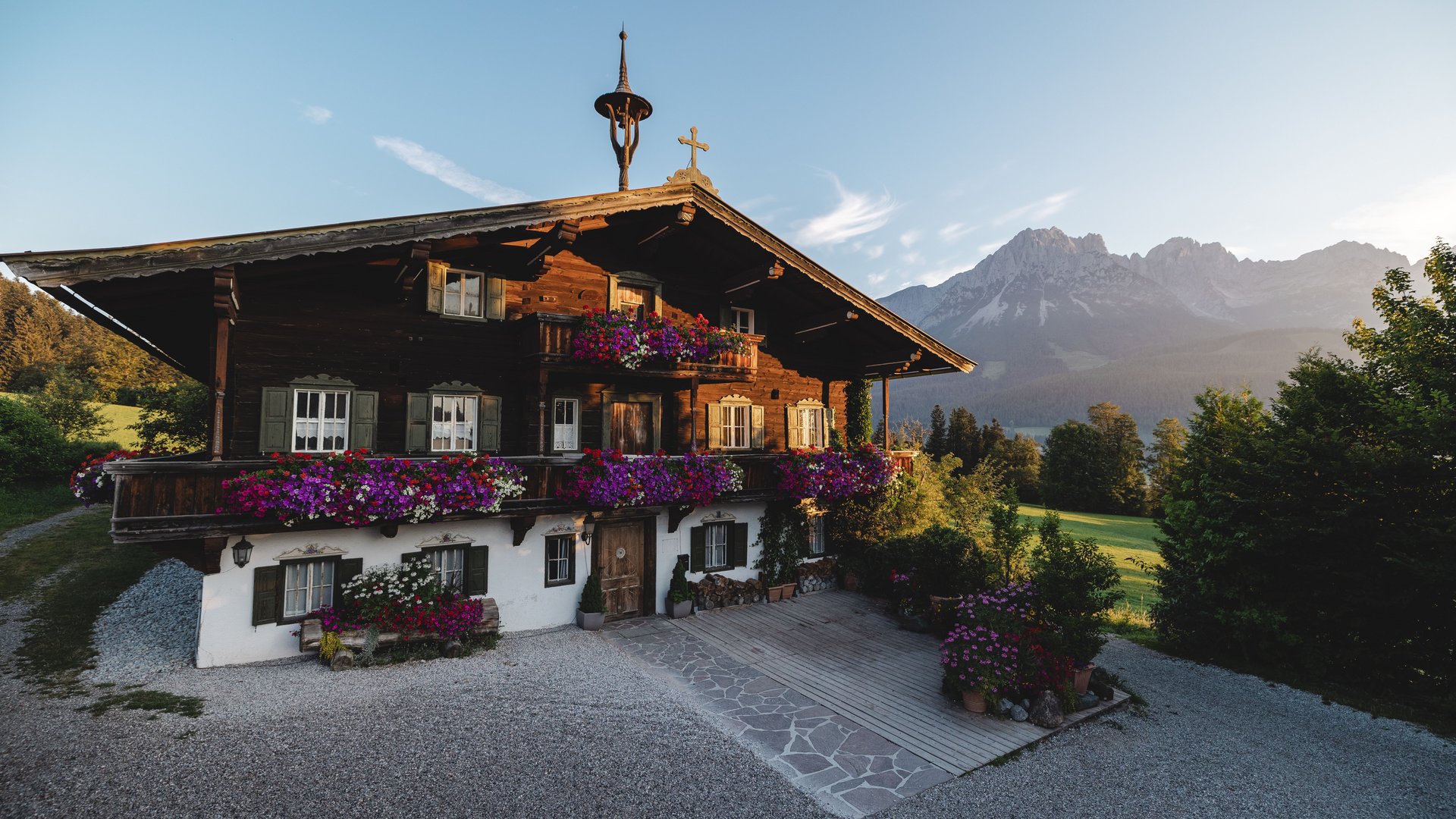 Die Drehorte von “Der Bergdoktor“ am Wilden Kaiser Traditionelles Holzhaus mit bunten Blumen und Alpen im Hintergrund bei Sonnenuntergang