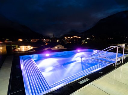 Der Postwirt: Hotel mit Infinitypool in Tirol Beleuchteter Außenpool bei Nacht mit Bergblick und Häusern im Hintergrund