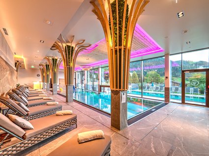 Der Postwirt: Hotel mit Infinitypool in Tirol Innenbereich eines Wellnesspools mit Liegestühlen und beleuchteten Holzsäulen