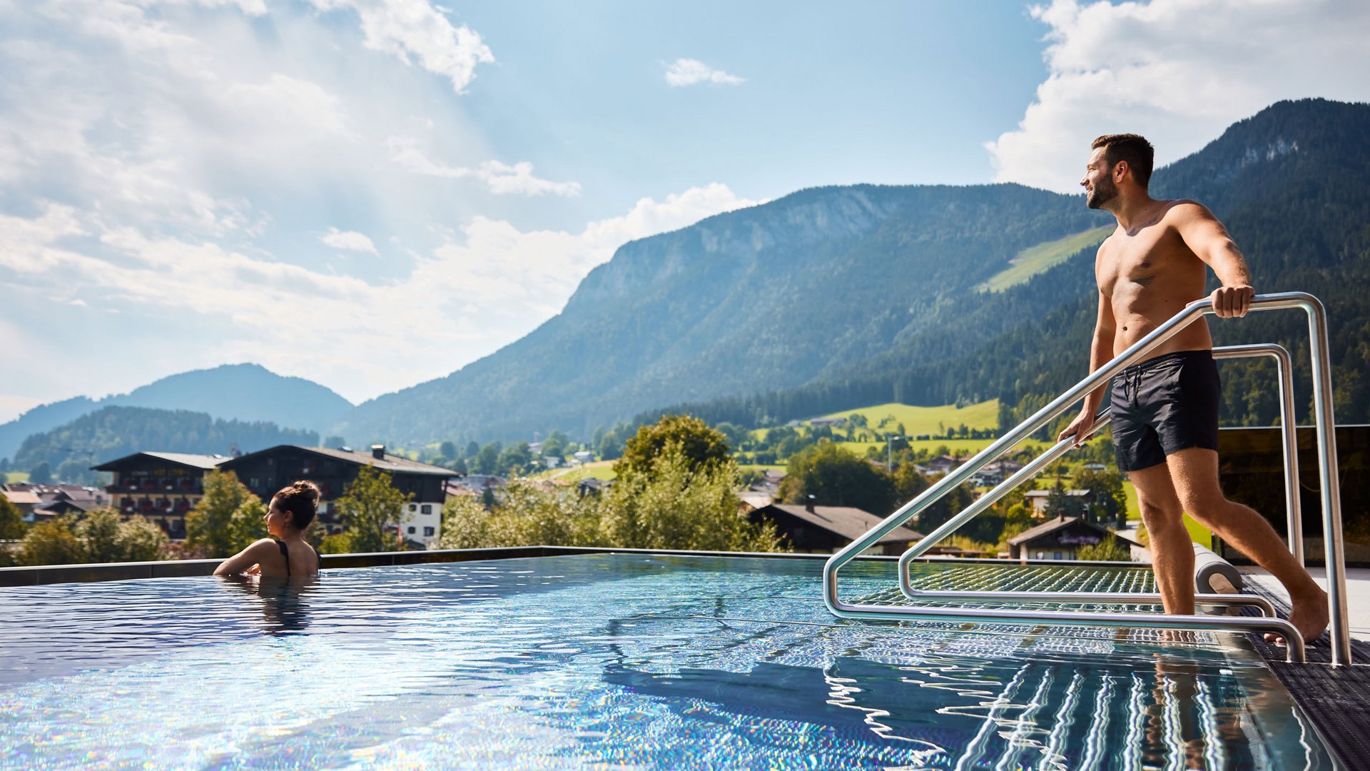 Sie suchen ein Wellnesshotel in Tirol für adults only? Mann steigt aus Pool mit Blick auf Berge, Frau entspannt im Wasser