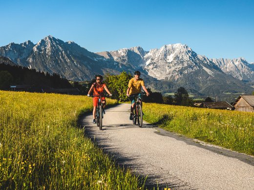 Sommer am Wilden Kaiser: Wandern und mehr Zwei Radfahrer auf Landstraße vor Berglandschaft mit grünen Wiesen und blühenden Blumen