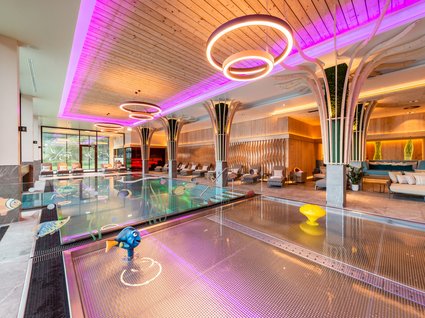 Moderner Indoor-Pool mit LED-Beleuchtung Ein großer, moderner Innenpool mit bunter LED-Deckenbeleuchtung und gemütlichen Liegen im Hintergrund, ideal für Entspannung und Erholung.