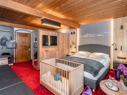 Hochwertige Ausstattung im Familienhotel am Wilden Kaiser Gemütliches Hotelzimmer mit Kinderbett, Doppelbett und Holzmöbeln