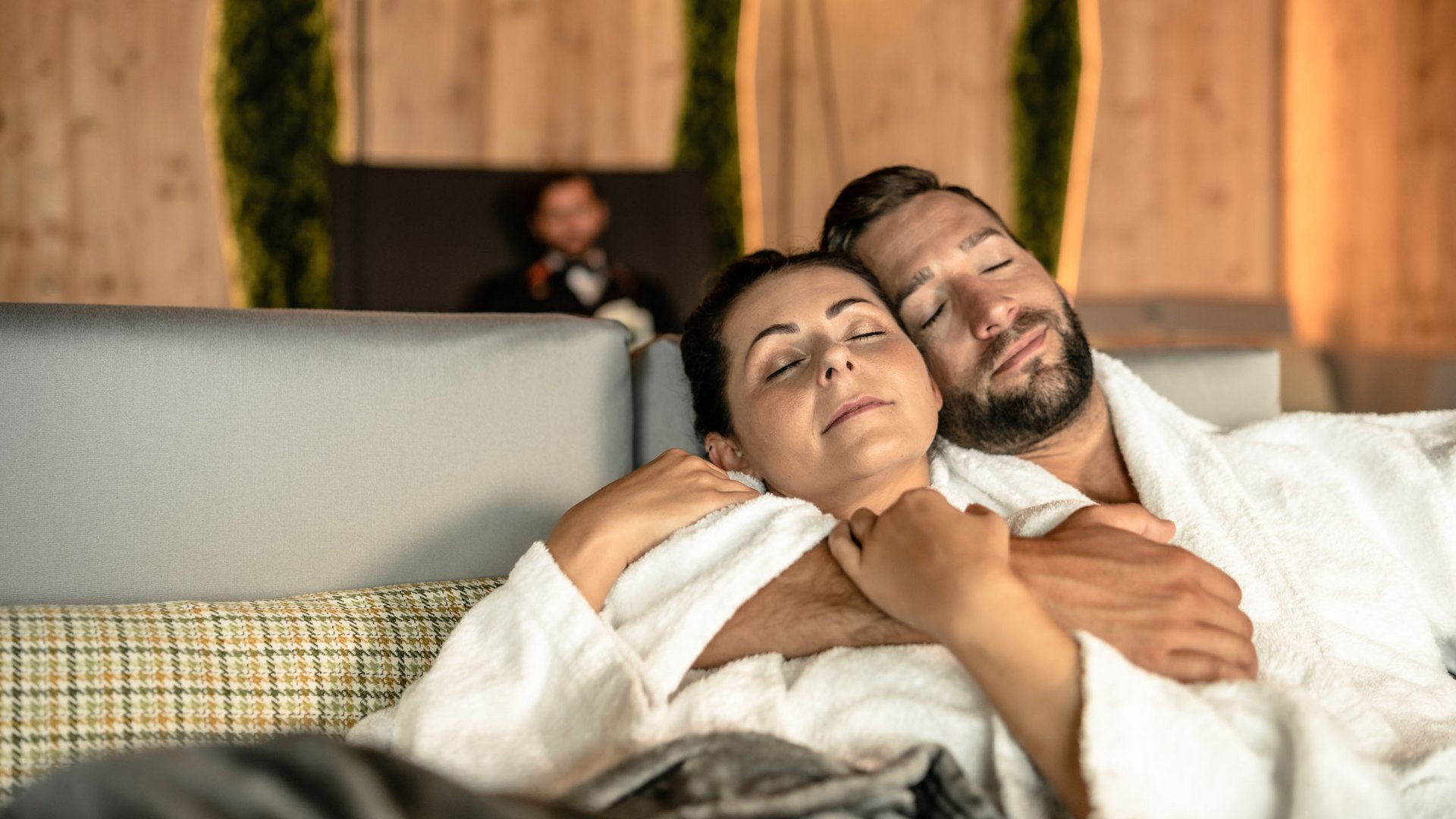 Sie suchen ein Wellnesshotel in Tirol für adults only? Paar entspannt in weißen Bademänteln auf Sofa, Augen geschlossen