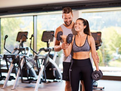 Fitnessstudio mit Hanteln Frau trainiert mit Kurzhanteln im Fitnessstudio mit Trainerunterstützung