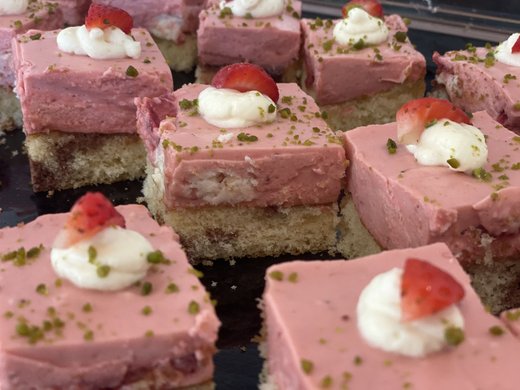Kulinarische Verführungen in unserem Hotel in Söll/Tirol Quadratische Erdbeer-Buttercreme-Kuchenstücke mit Sahne und Pistazien bestreut