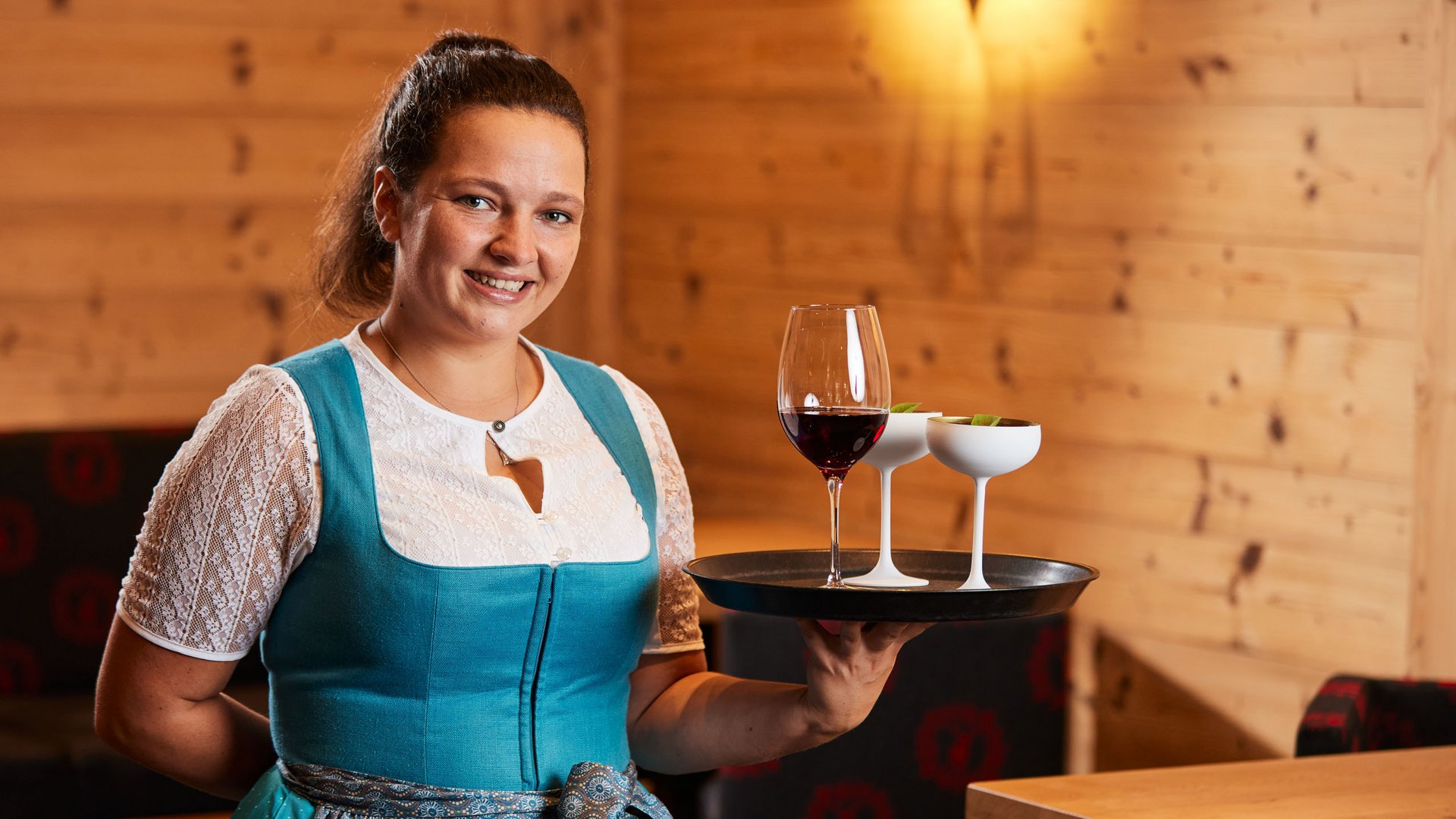Arbeiten im Postwirt Kellnerin in traditioneller Kleidung trägt Tablett mit drei Getränken in einem Holzrestaurant