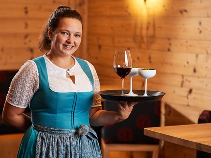 Arbeiten im Postwirt Kellnerin in traditioneller Kleidung trägt Tablett mit drei Getränken in einem Holzrestaurant