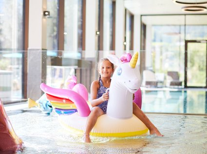 Der Postwirt: Hotel mit Infinitypool in Tirol Mädchen auf einem aufblasbaren Einhorn im Hallenbad
