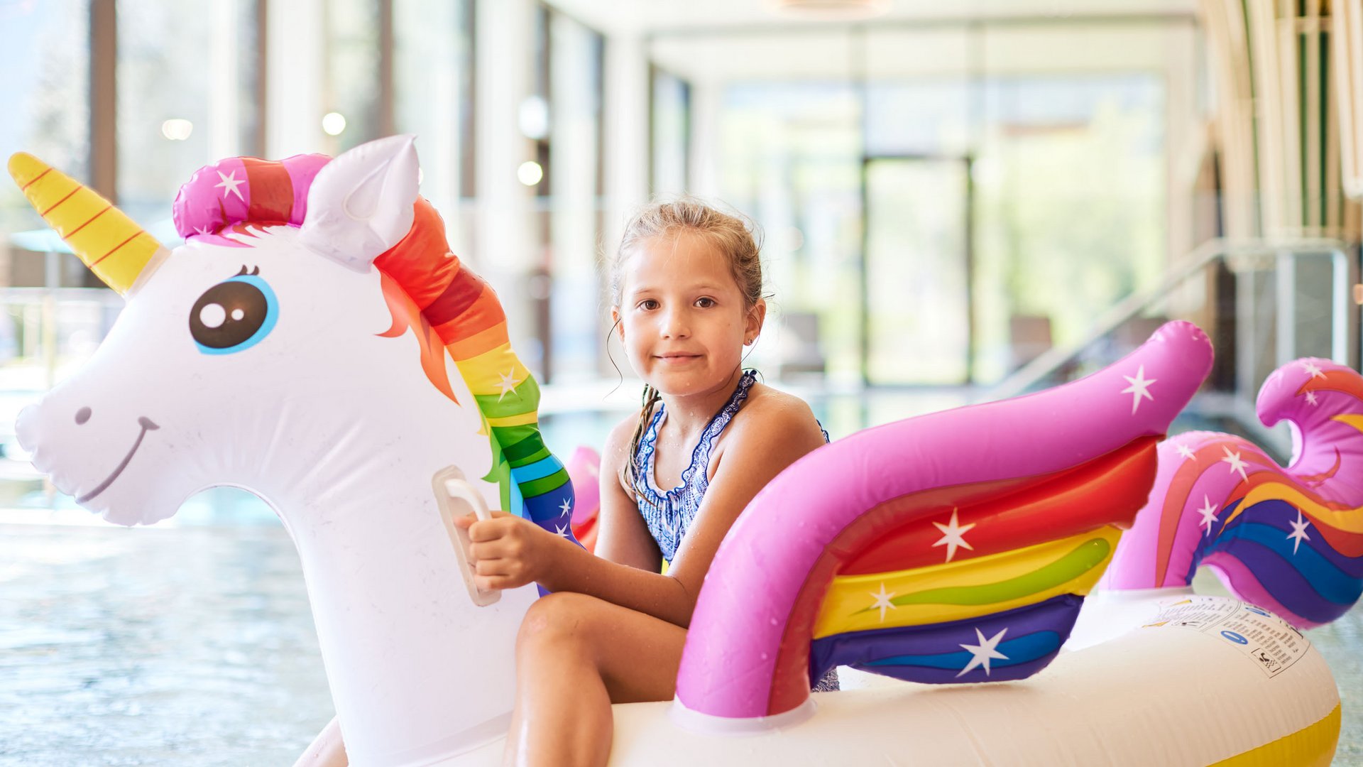 Hochwertige Ausstattung im Familienhotel am Wilden Kaiser Mädchen auf aufblasbarem Einhorn im Hallenbad
