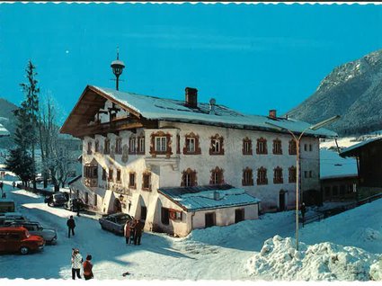 Unser Hotel in Söll/Österreich: eine spannende Geschichte Schneebedecktes traditionelles Alpenhaus mit Menschen und Autos in einem Bergdorf