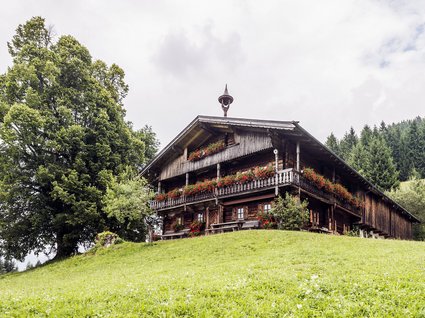 Entdecken Sie die Region mit der Wilder Kaiser GästeCard! Altes Holzhäuschen mit Blumengirlanden auf einem grünen Hügel