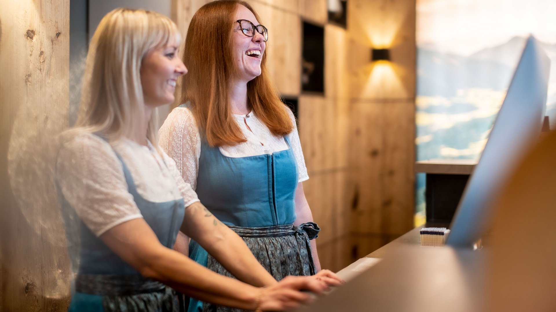Hotel in Söll am Wilden Kaiser: der Postwirt Zwei Frauen in Trachten lachen am Empfangstresen eines Hotels